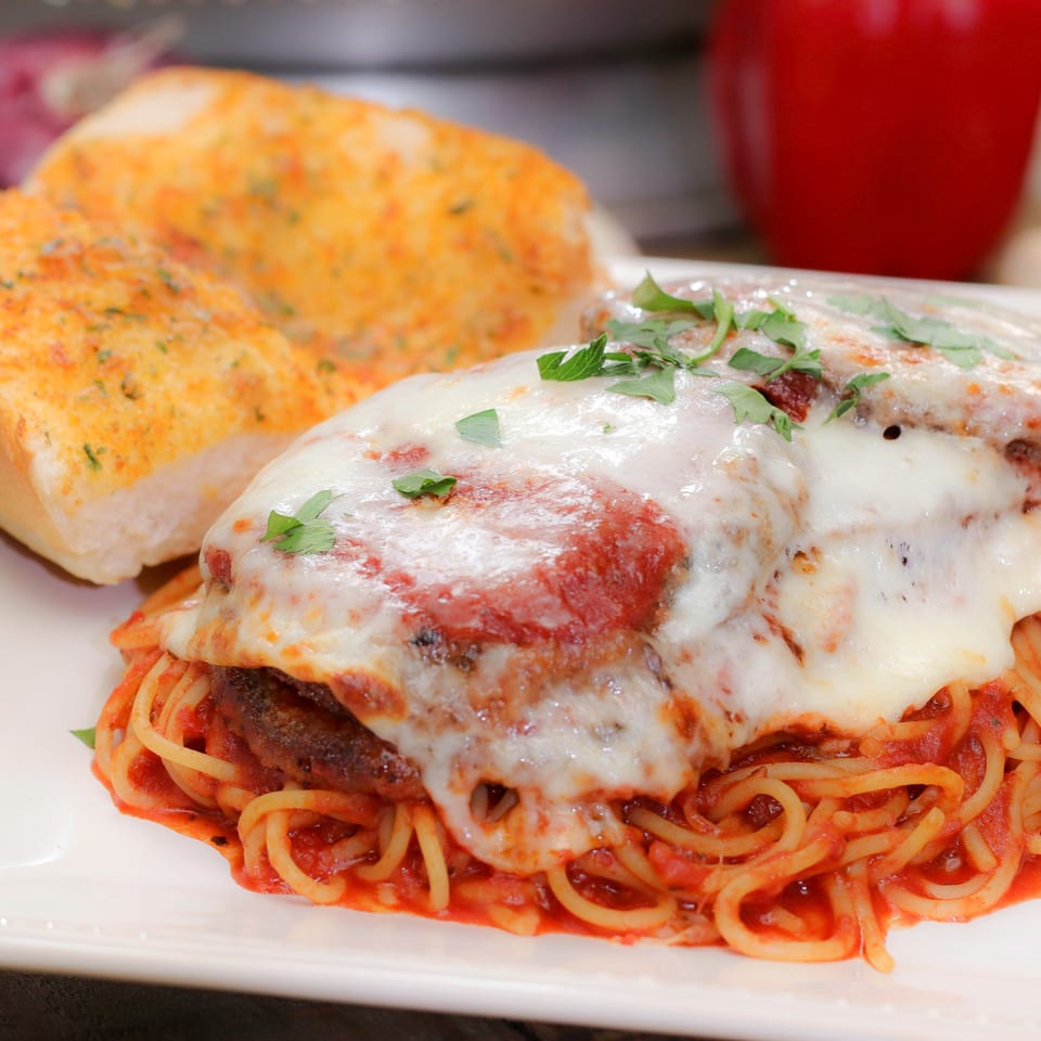 Spaghetti with meatballs, melted cheese, and tomato sauce, served with garlic bread.