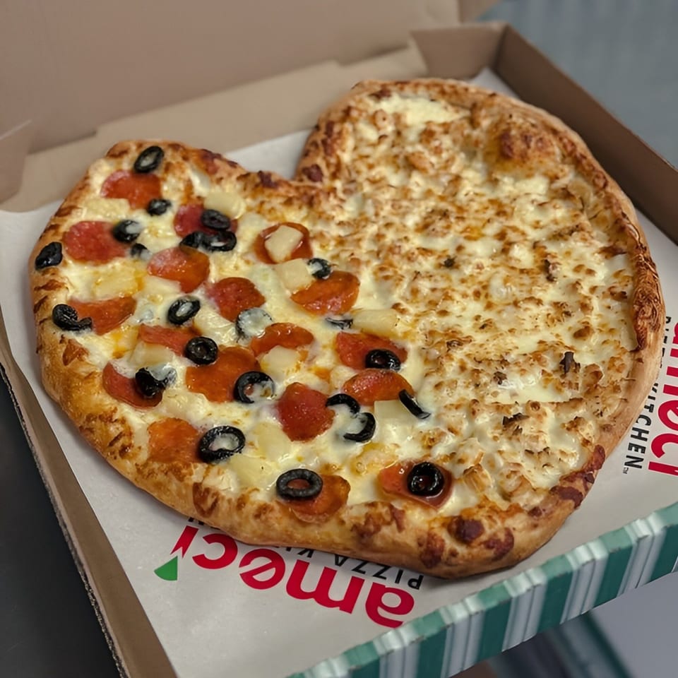 Heart-shaped Ameci Pizza with pepperoni, olives, pineapple on one side, and white sauce chicken on the other.